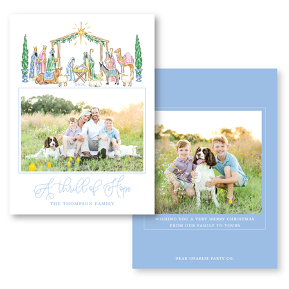 The image is a holiday card featuring a family portrait of a man, woman, and two children, along with a nativity scene and a dog. The card has a blue background with white text and graphics.
