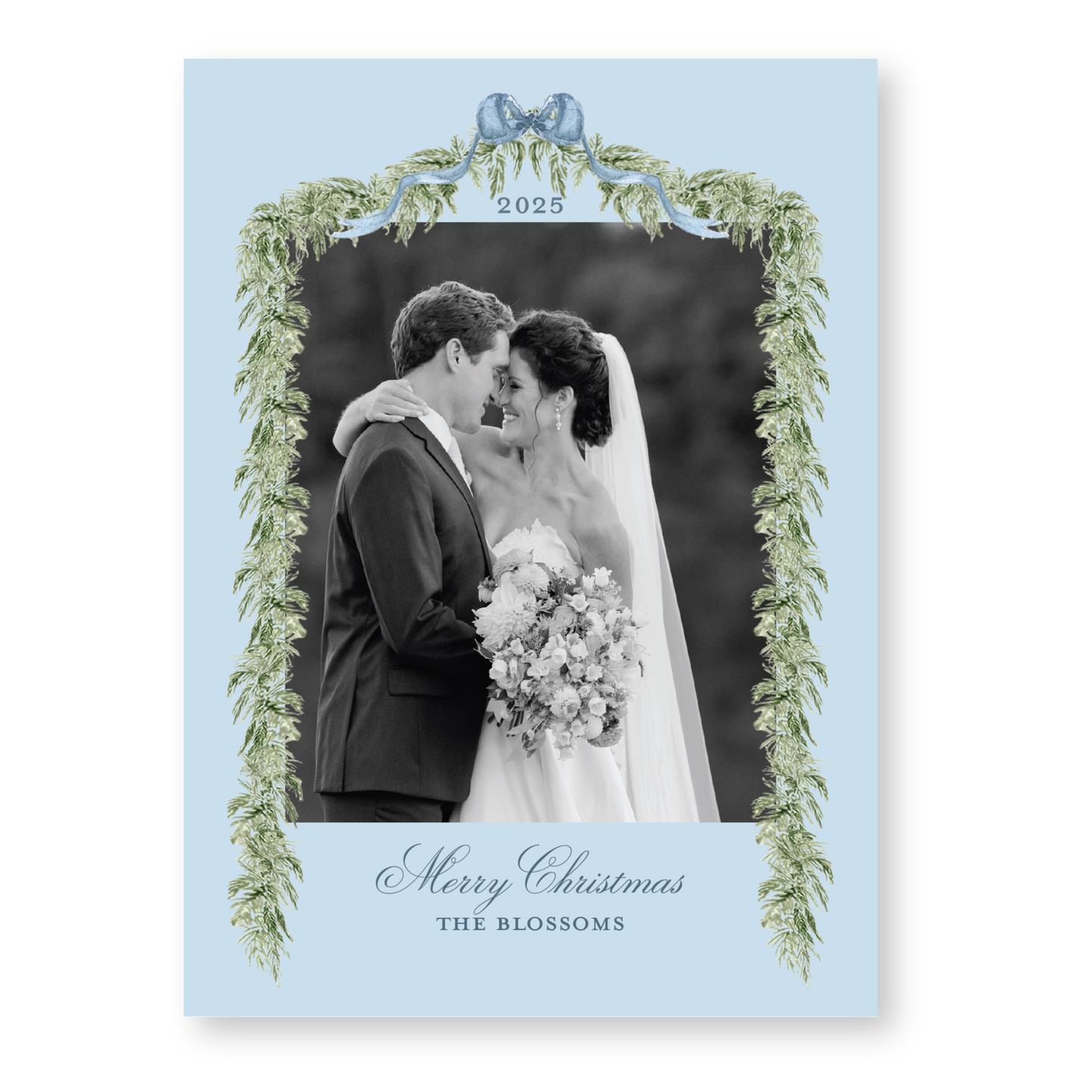 A black and white photograph of a couple embracing, with a decorative border of greenery and the text "Merry Christmas" and "The blossoms" below the couple.