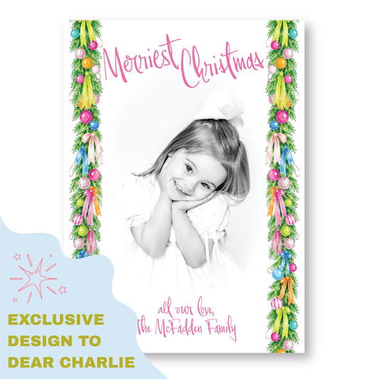 A black and white photograph of a young girl with a warm smile, framed by a colorful border with Christmas ornaments and greenery. The text "Merry Christmas" is written above the girl's head, and "all our love, The McFadden Family" is written below her. The image also includes a text that says "EXCLUSIVE DESIGN TO DEAR CHARLIE".