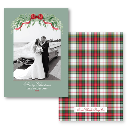The image is a wedding card featuring a bride and groom standing together in front of a car, with a festive wreath above them. The card has a green background and a red ribbon.