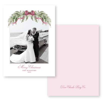 A black and white photograph of a bride and groom standing next to a car, with a pink ribbon and greenery decoration above them. The text below the image reads "Merry Christmas THE BLOSSOMS 2015".