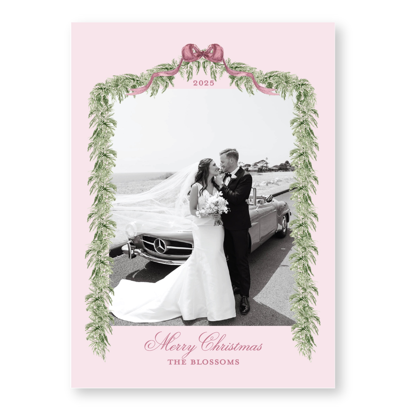 A black and white photo of a bride and groom standing next to a car, framed by a decorative border with greenery and a pink ribbon.