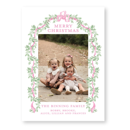 three young children sitting together on a path, surrounded by a decorative border with pink and green leaves. The text "Merry Christmas" is displayed above the children, and "THE BINNING FAMILY" is written below them.