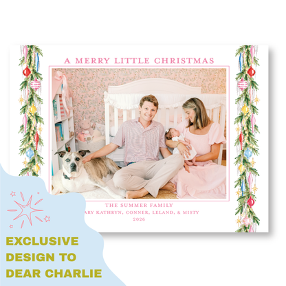 A family portrait of a couple and their newborn baby, with a dog in the background, is displayed in a frame. The text "A MERRY LITTLE CHRISTMAS" is written above the photo, and "THE SUMMER FAMILY" is written below the photo. The text "EXCLUSIVE DESIGN TO DEAR CHARLIE" is written at the bottom of the image.