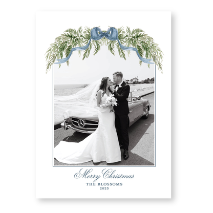 A black and white photograph of a bride and groom standing next to a car, with a decorative floral arch above them. The text at the bottom of the image reads "Merry Christmas THE BLOSSOMS 2028".