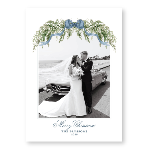 A black and white photograph of a bride and groom standing next to a car, with a decorative floral arch above them. The text at the bottom of the image reads "Merry Christmas THE BLOSSOMS 2028".
