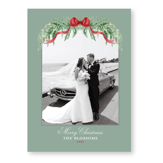 A black and white photograph of a bride and groom standing next to a car, with a festive wreath and red ribbon above them. The text at the bottom of the image reads "Merry Christmas THE BLOSSOMS 2015".