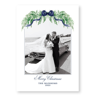 A black and white photograph of a bride and groom standing next to a car, with a festive wreath and ribbon decoration above them. The text at the bottom of the image reads "Merry Christmas THE BLOSSOMS 2015".