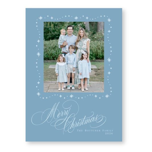 A family portrait of a man, woman, and three children dressed in light blue clothing, standing together in a garden setting. The text &quot;Merry Christmas&quot; is written in a decorative font at the bottom of the image, and &quot;The Botcher Family&quot; and &quot;2024&quot; are written in smaller text at the bottom right corner.