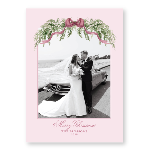 A black and white photo of a bride and groom standing next to a car, with a pink floral border and the text "Merry Christmas" and "THE BLOSSOMS" below.