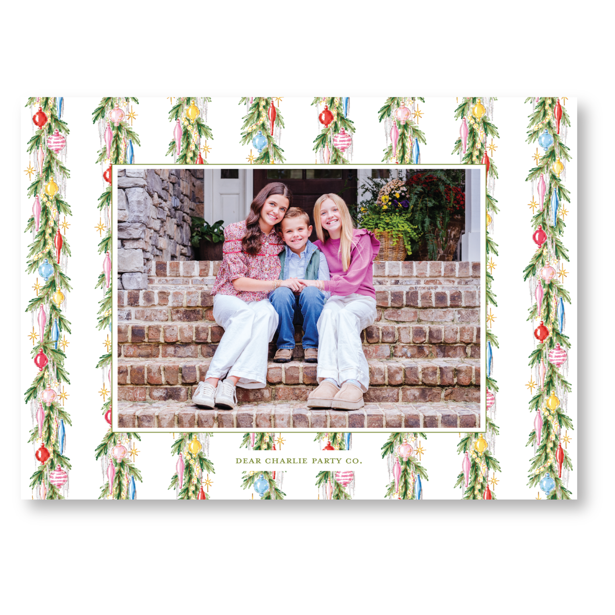 A family of three, consisting of two women and a child, is sitting together on a set of stairs, with a festive holiday decoration pattern surrounding them.