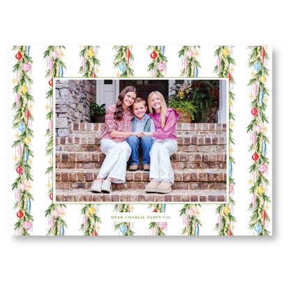 A family of three, consisting of two women and a child, is sitting together on a set of stairs, with a festive holiday decoration pattern surrounding them.